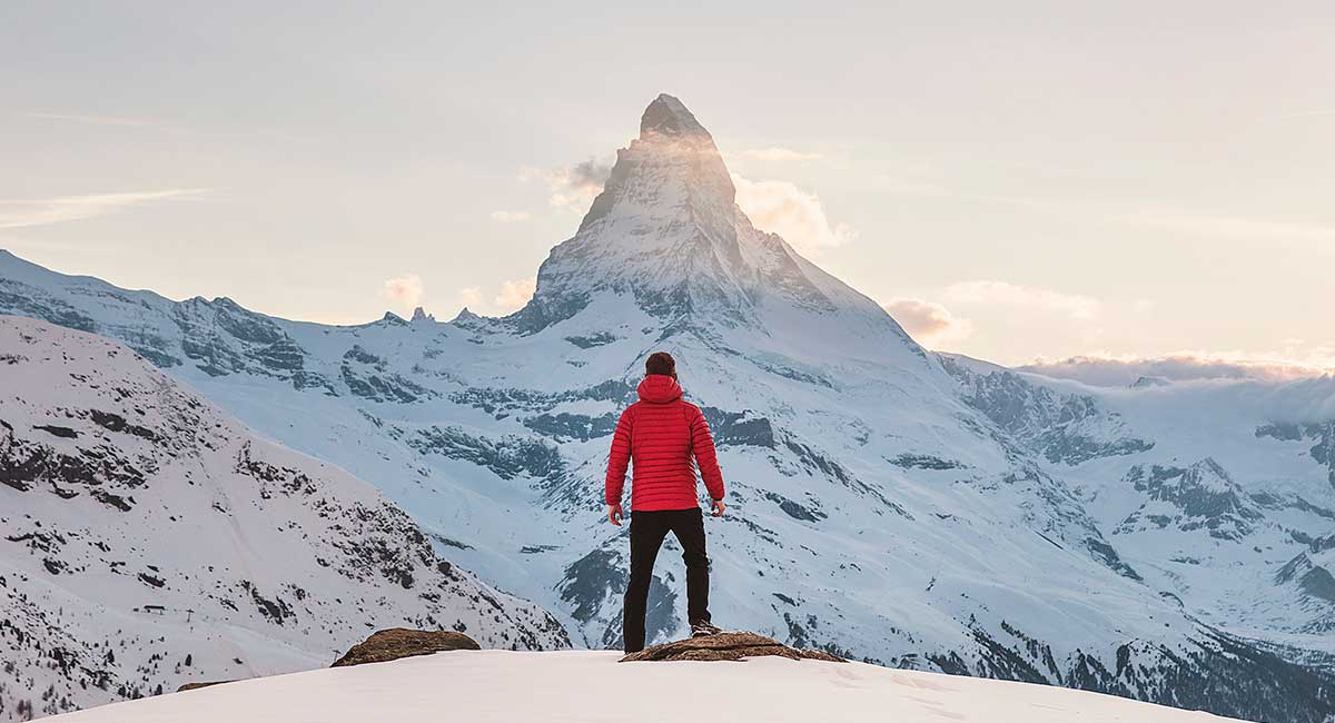 Ein Mann steht auf einer Felskuppe und sieht sein Ziel, die Bergspitze, vor sich. Lerne mit NLP wie du alles erreichen kannst, was du möchtest.